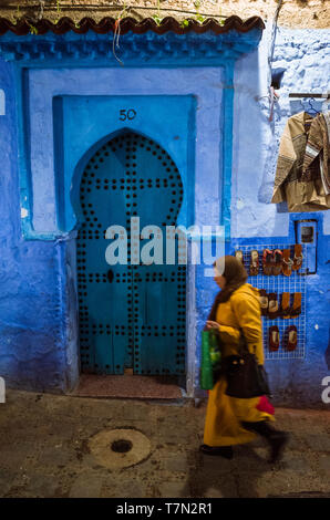 Chefchaouen, Maroc : une femme passe devant une porte en bois traditionnel dans le bleu à la chaux medina vieille ville de nuit. Banque D'Images