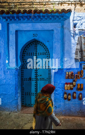 Chefchaouen, Maroc : une femme passe devant une porte en bois traditionnel dans le bleu à la chaux medina vieille ville de nuit. Banque D'Images