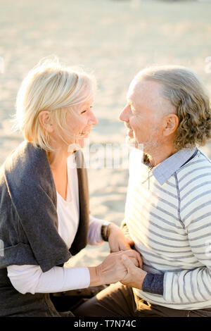 Personnes âgées smiling caucasian couple holding hands épouse et assis sur la plage de sable. Concept d'heureux retraités sur pique-nique. Banque D'Images