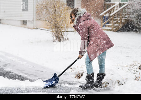 Jeune femme en robe d'hiver pelletage de nettoyage de rue allée dans la neige Tempête de neige lourde holding pelle par maison d'habitation Banque D'Images