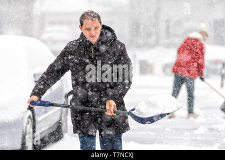 Heureux jeune homme en manteau d'hiver pelletage de nettoyage de rue allée couverte de chute de neige dans une tempête de neige lourde avec pelle Banque D'Images