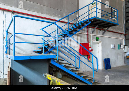 Échelle en métal bleu dans une ancienne usine. La boîte du feu rouge et le feu sur la paroi du tube. Banque D'Images