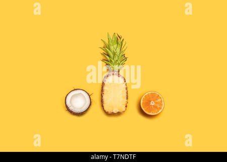 L'été créatif composition de jus de fruits tropicaux sur un fond jaune : oranges, citrons, noix de coco, l'ananas. Banque D'Images