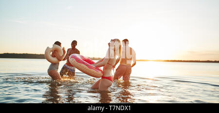 Rire de groupe divers jeunes amis des maillots unis dans un lac au coucher du soleil de rire et de projections d'eau à chaque autre Banque D'Images