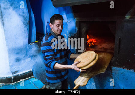 Chefchaouen, Maroc : Un homme cuit le pain dans un four traditionnel dans le bleu à la chaux medina vieille ville. Banque D'Images