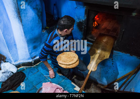 Chefchaouen, Maroc : Un homme cuit le pain dans un four traditionnel dans le bleu à la chaux medina vieille ville. Banque D'Images