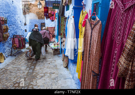 Chefchaouen, Maroc : deux femmes passent devant les magasins de vêtements traditionnels dans le bleu à la chaux medina vieille ville. Banque D'Images