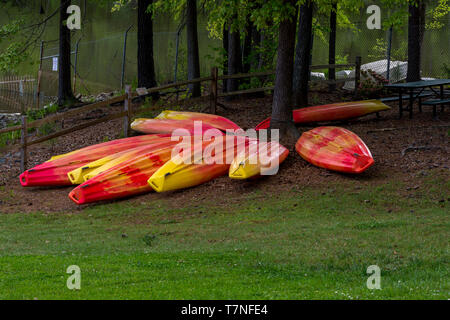 L'orange et le jaune des kayaks stocké à l'envers sur l'herbe avec le lac en arrière-plan Banque D'Images