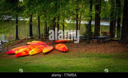 L'orange et le jaune des kayaks stocké à l'envers sur l'herbe avec le lac en arrière-plan Banque D'Images