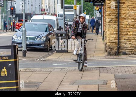 Jeune homme équitation sa moto sur le trottoir le long de Wellingborough Rd, Northampton, Royaume-Uni. Banque D'Images