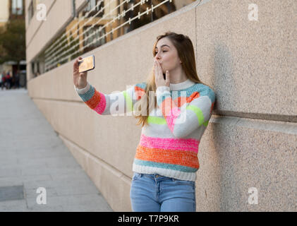 Heureux jolie fille adolescente à l'aide de smart mobile phone heureux soufflant un baiser et forme à des disciples des amis ou de la famille de l'enregistrement vidéo et de chatter. Vide Banque D'Images