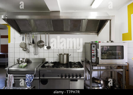 Système de cuisson en acier inoxydable avec des plaques de cuisson, grill, four et hotte aspirante dans une cuisine de cantine professionnelle Banque D'Images