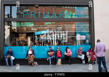 Avril 2019 à Londres. Le Shopping, Oxford Street. Shoppers prendre un repos à l'extérieur de Primark et certains vérifier leurs téléphones Banque D'Images