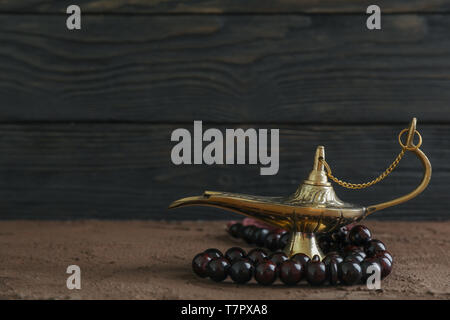 Lampe Aladdin magique avec chapelet sur table en bois brun contre l'arrière-plan Banque D'Images