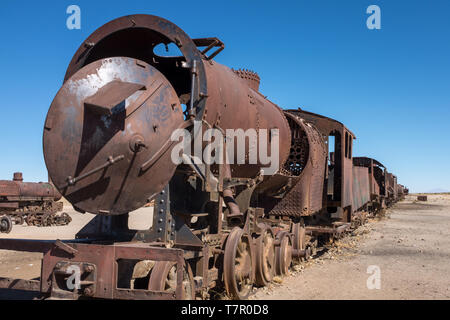 Vue sur le côté d'un train à vapeur et wagons rouillés pourrissent lentement à la cimetière juste à l'extérieur d'Uyuni, Bolivie, contre un ciel bleu. Banque D'Images