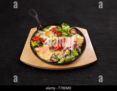 Les oeufs au plat avec du bacon frit croustillant, salade et tomates en fry pan Banque D'Images