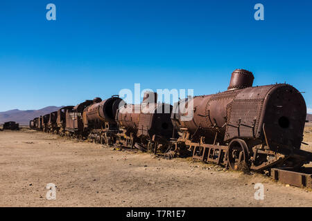 La rouille des trains à vapeur et des voitures pourrissent lentement à la cimetière juste à l'extérieur d'Uyuni, Bolivie, contre un ciel bleu. Banque D'Images