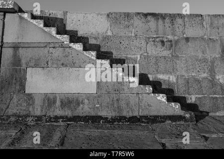 Vieux escaliers de pierre sur la Lyme Regis Cobb, tourné en noir et blanc avec des ombres contre le mur de pierre. Banque D'Images