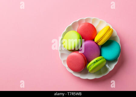 Macarons dessert sur assiette blanche. Arrière-plan de couleur pastel rose. Vue d'en haut. Copier l'espace. Banque D'Images