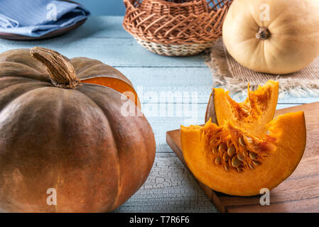 Les imperfections naturelles avec les citrouilles et graines de citrouille avec des tranches sur une planche à découper et sur la surface en bois bleu. Chiffon et panier à l'arrière-plan. Selecti Banque D'Images