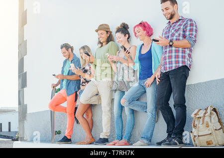 Les jeunes gens à l'écoute sur leurs téléphones mobiles intelligents s'appuyant sur un mur - Génération accro aux nouvelles technologies Banque D'Images