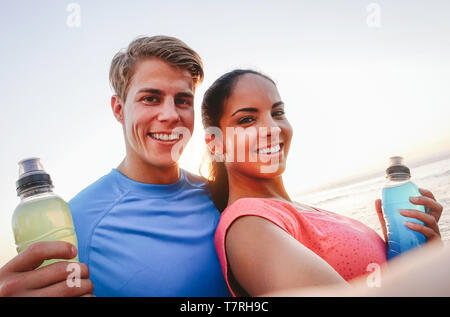 Couple sportif en tenant un téléphone mobile avec selfies au coucher du soleil - les jeunes d'avoir une pause de la formation et de boire des boissons énergétiques Banque D'Images