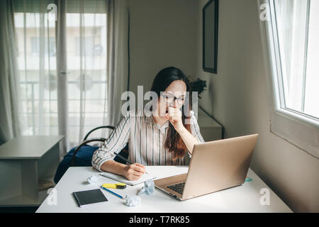 Une fille travaille à un ordinateur dans un bureau à domicile ou un étudiant de l'enseigne accueil leçons. Elle est fatiguée, bâillements et veut dormir ou s'ennuie. Banque D'Images