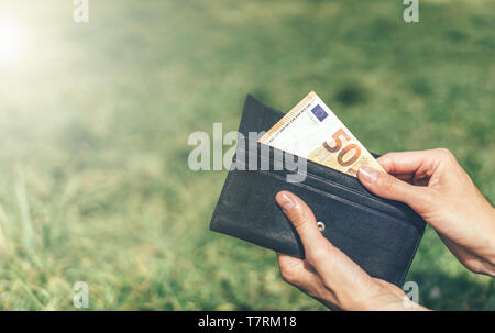 Close-up hands sort un billet de 50 euros à partir d'une pochette sur fond vert à l'extérieur Banque D'Images