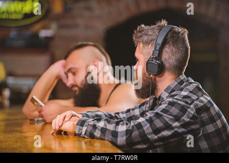 Fuir la réalité. Vendredi détente dans un bar. Hipster barbu dépenser à loisir comptoir bar. Commander des boissons au bar. Les hommes avec des écouteurs et smartphone détente à bar. Éviter la communication. Banque D'Images