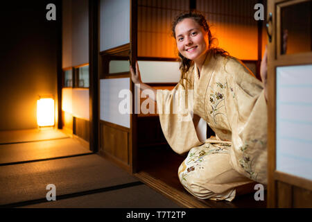 Maison traditionnelle japonaise ou ryokan avec gaijin caucasian woman en kimono et chaussettes tabi ouverture coulissante portes papier shoji assis sur tatamis cheminée Banque D'Images