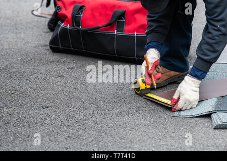 La construction de gros plan homme mesurant des bardeaux de toiture avec du ruban d'asphalte sur la rue allée au sol Banque D'Images