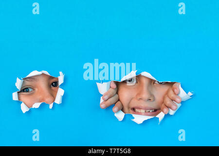 Les jeunes enfants curieusement peeking through hole dans du papier copie espace au-dessus pour le texte. Banque D'Images