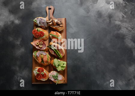 Brushetta ou des tapas espagnoles traditionnelles. Hors-d'antipasti italiens avec des collations. Variété de petits sandwichs au jambon, tomates cerises, du saumon Banque D'Images