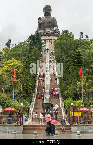 Hong Kong, Chine - mars 7, 2019 : l'île de Lantau. Tian Tan Buddha statue géante sur le dessus de la colline couverte d'arbres avec escalier marron sous le ciel de pluie. F Rouge Banque D'Images