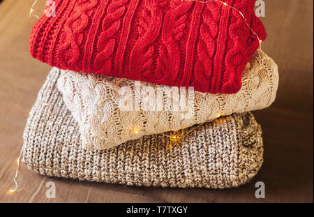 Une pile de pulls sur le fond tissu marron décoré de lumières. Des vêtements confortables. Banque D'Images