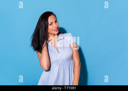 Young woman wearing dress isolés sur le mur bleu cheveux touchant à la caméra ludique smiling Banque D'Images