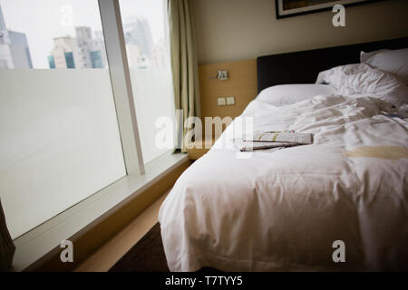 Couché sur journal un lit défait dans une chambre d'hôtel. Banque D'Images