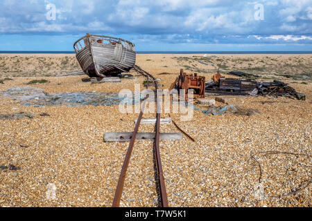 Old rusty voie ferrée sur une grande plage de galets plats menant à un vieux bateau de pêche en bois qui est assis sur la plage, éparpillés sur la plage sont lo Banque D'Images