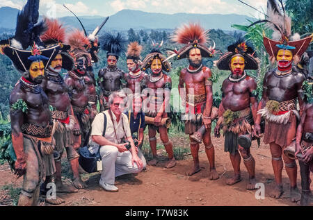 Deux Américains posent pour une photo avec le Huli Wigmen le couple avait photographié au cours d'une cérémonie traditionnelle de chanter chanter au Tari dans les hautes terres du sud de la Papouasie-Nouvelle-Guinée (PNG), une télécommande et des pays dans l'océan Pacifique au large de la pointe nord-est de l'Australie. Avant de frapper leurs petits tambours et la danse à l'unisson, ces guerriers masculins passent des heures à décorer eux-mêmes par peindre les visages et les corps et wearing hat-comme les perruques ornée de plumes colorées. Chantez-chante dans le passé étaient souvent préludes à des guerres tribales, mais de nos jours de détente pour les autochtones et les touristes. Banque D'Images