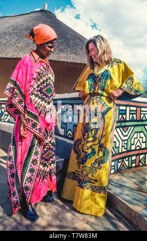 Une femme sud-africaine et d'un American Woman admirer les créations artistiques à la mode de couleur deux robes de pleine longueur à vendre à un magasin d'artisanat Bantou près de Pretoria, la capitale de l'administration de l'Afrique du Sud. Banque D'Images