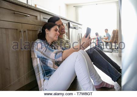 Affectionate couple using smart phone sur le plancher de la cuisine avec les enfants en arrière-plan