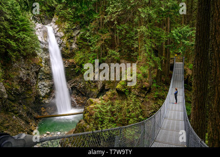 Femme debout sur un pont suspendu et regarder les chutes Cascade, dans le parc régional des chutes Cascade, Deroche, British Columbia, Canada Banque D'Images