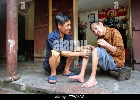 L'Agent Orange victime Minh Long Nguyen (64, à droite) est pris en charge par son voisin Van Hung (54). Village de Phu Ly Nam Ha (province) près de Hanoi, Vietnam Banque D'Images