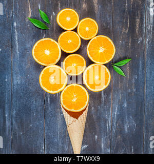 Plat à l'obscurité créative jeter Vue de dessus des tranches de fruits d'orange dans la crème glacée cornet gaufré sur fond de table en bois brun avec copie espace. Un minimum de Banque D'Images
