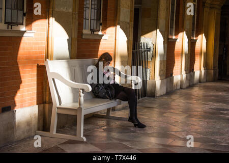 Lady est assise sur un banc en bois dans l'ombre de son téléphone portable à Hampton court Banque D'Images