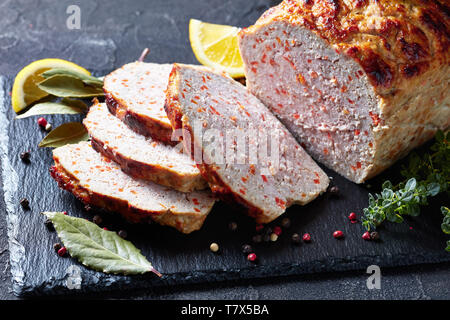 Pain de viande de poulet en tranches sur un plateau en ardoise noire avec les tranches de citron et thym frais sur une table, vue horizontale à partir de ci-dessus, close-up Banque D'Images