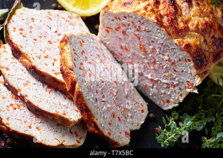 Close-up de tranches de pain de viande de poulet sur une plaque en ardoise noire avec les tranches de citron et thym frais sur une table horizontale de béton, vue de dessus, mac Banque D'Images