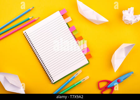 Le bloc-notes blanc vierge avec papiers, crayons et ciseaux sur fond jaune Banque D'Images