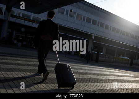 Un homme d'affaires en tirant un chariot à marcher vers l'entrée de l'aéroport pour prendre son vol tôt le matin Banque D'Images