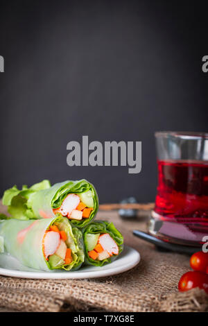 Rouleaux de salade sur assiette blanche placée sur un sac il y a la tomate et l'eau rouge en verre placé à côté. Banque D'Images